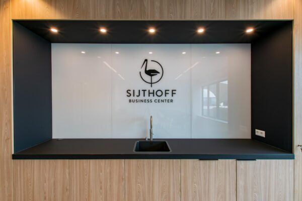 Moderne kitchenette met zwart werkblad en het logo van Sijthoff Business Center op een glanzende witte achterwand.